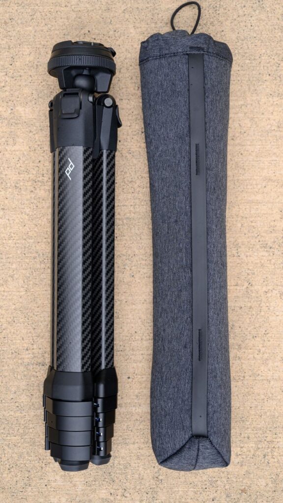 Folded Peak Design Carbon Fiber Travel Tripod next to its soft carry case on concrete surface.

