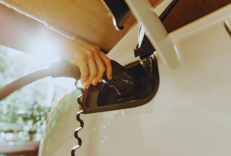 Hand plugging EV charger into electric car under sunlight, highlighting 2025 deals and expiring tax credits.
