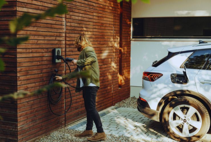 Home electric car charging station with person plugging in a white EV—representing 2025 deals and expiring federal tax credits.

